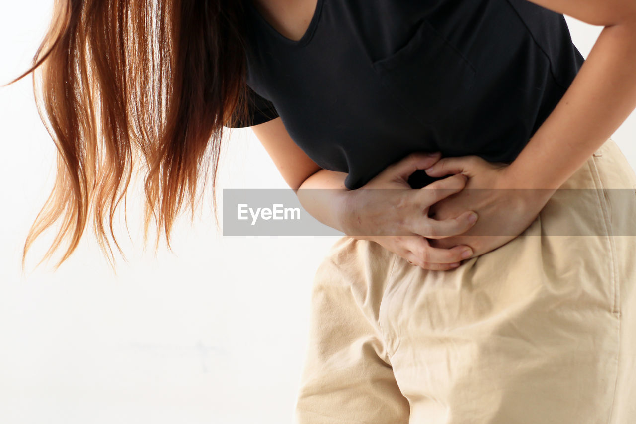 Midsection of woman suffering from stomachache against white background