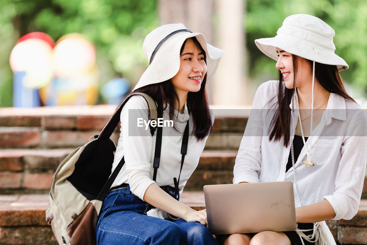 Woman looking away while sitting with laptop by friend