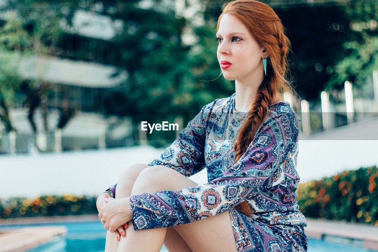 Close-up of young woman with hugging knees sitting on poolside