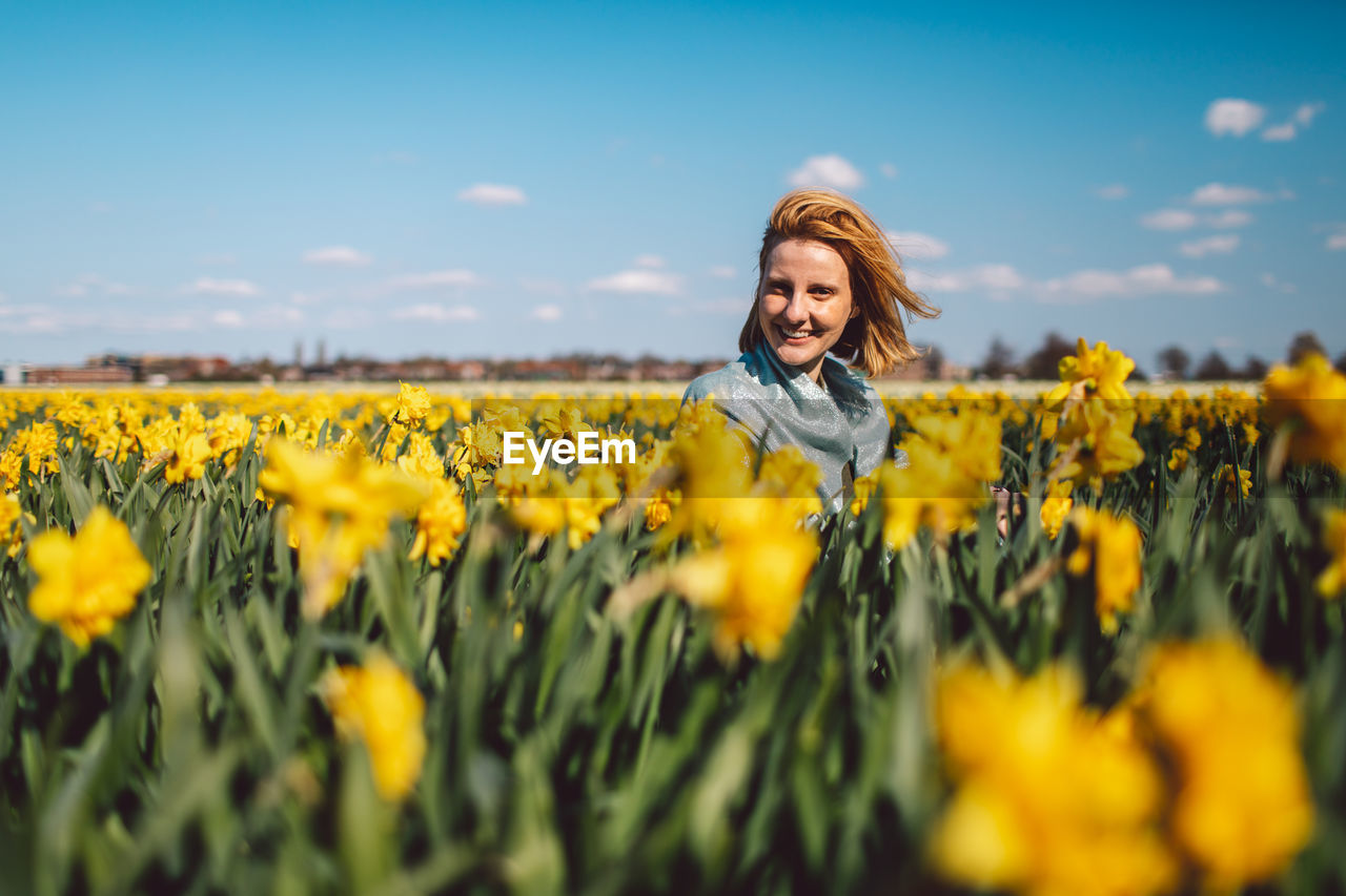 Portrait of smiling woman on narcissus field against sky