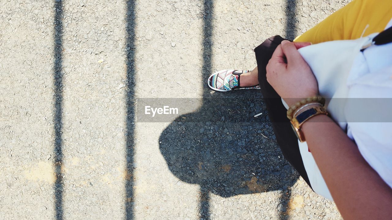Low section of woman walking on road during sunny day