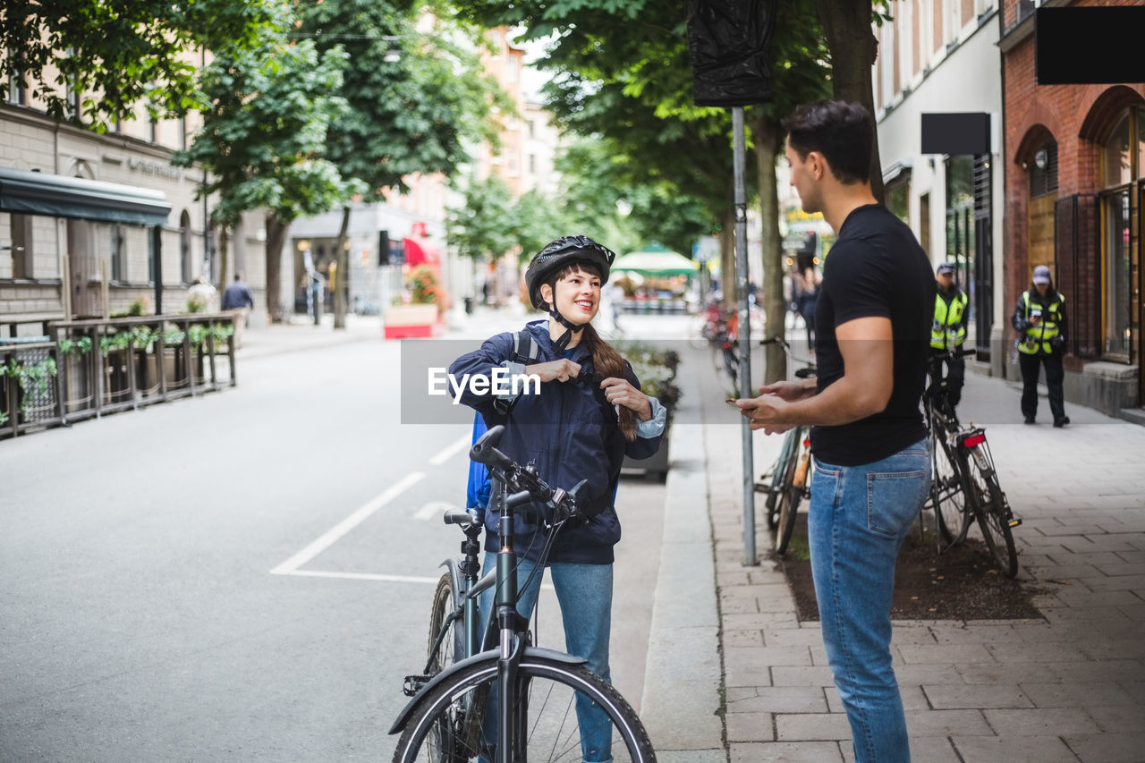 Delivery woman talking with male customer standing on sidewalk in city
