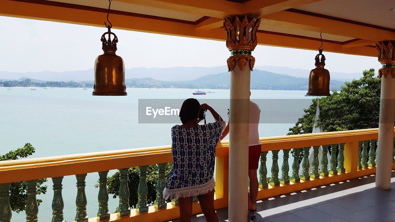 REAR VIEW OF WOMAN SITTING ON RAILING