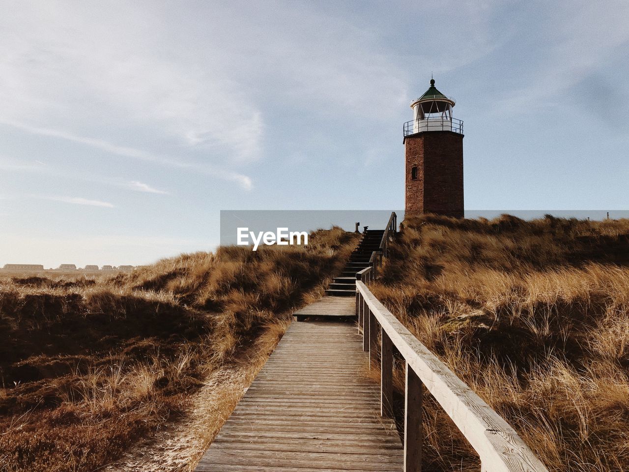 Footpath leading towards lighthouse amidst buildings against sky