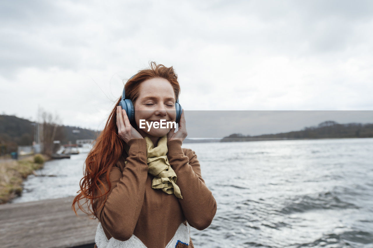 Smiling woman listening to music with eyes closed by lake