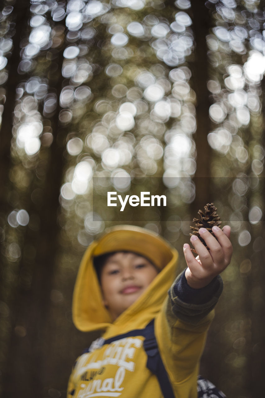 Portrait of smiling boy holding pine cone in forest