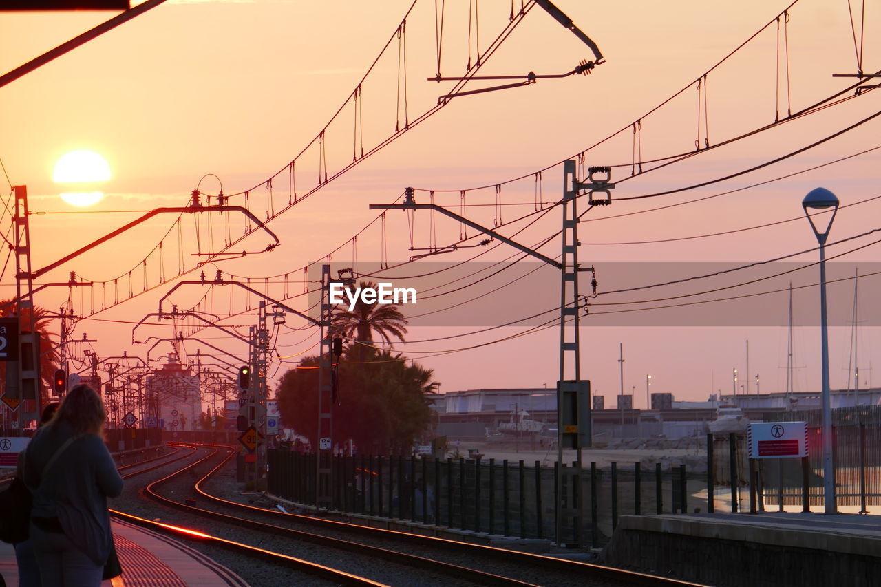 Railroad tracks in city against sky during sunset