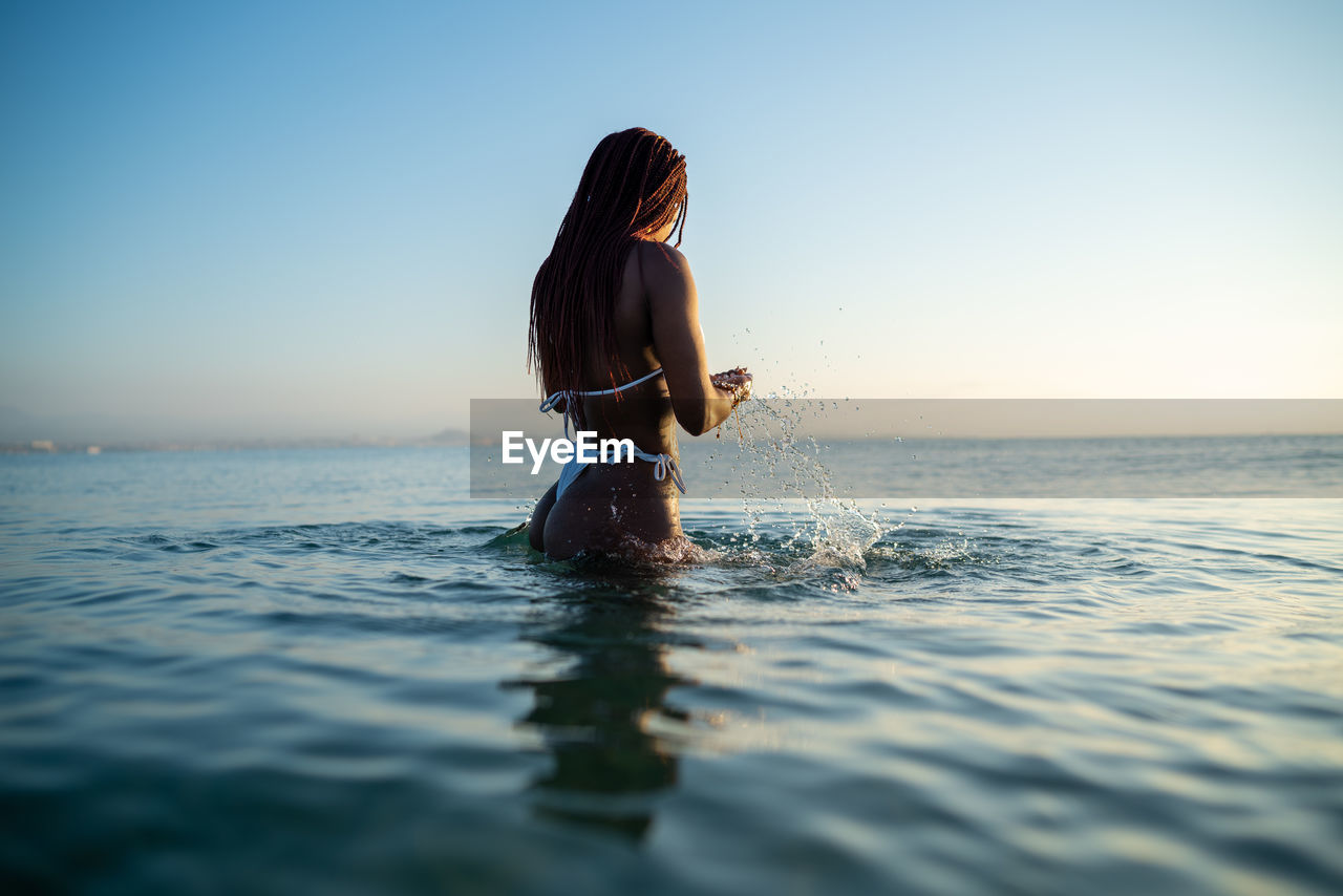 Back view anonymous black woman with braids on the beach