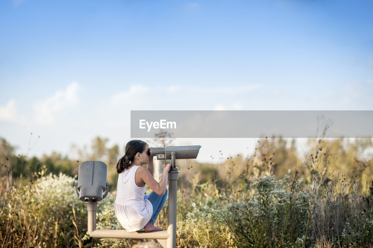 Teen girl looking out at nature through a telescope