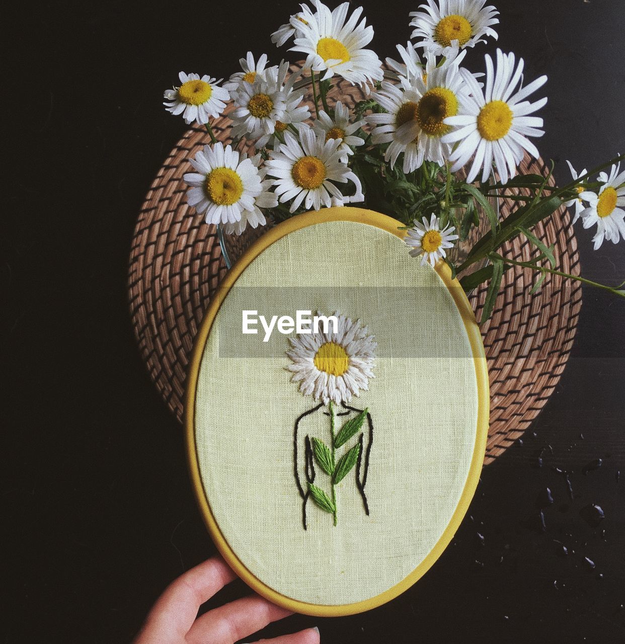 Close-up of hand holding embroidery art over white flowering plants