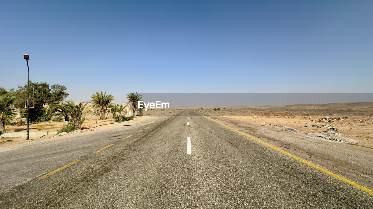 empty road amidst field against clear sky