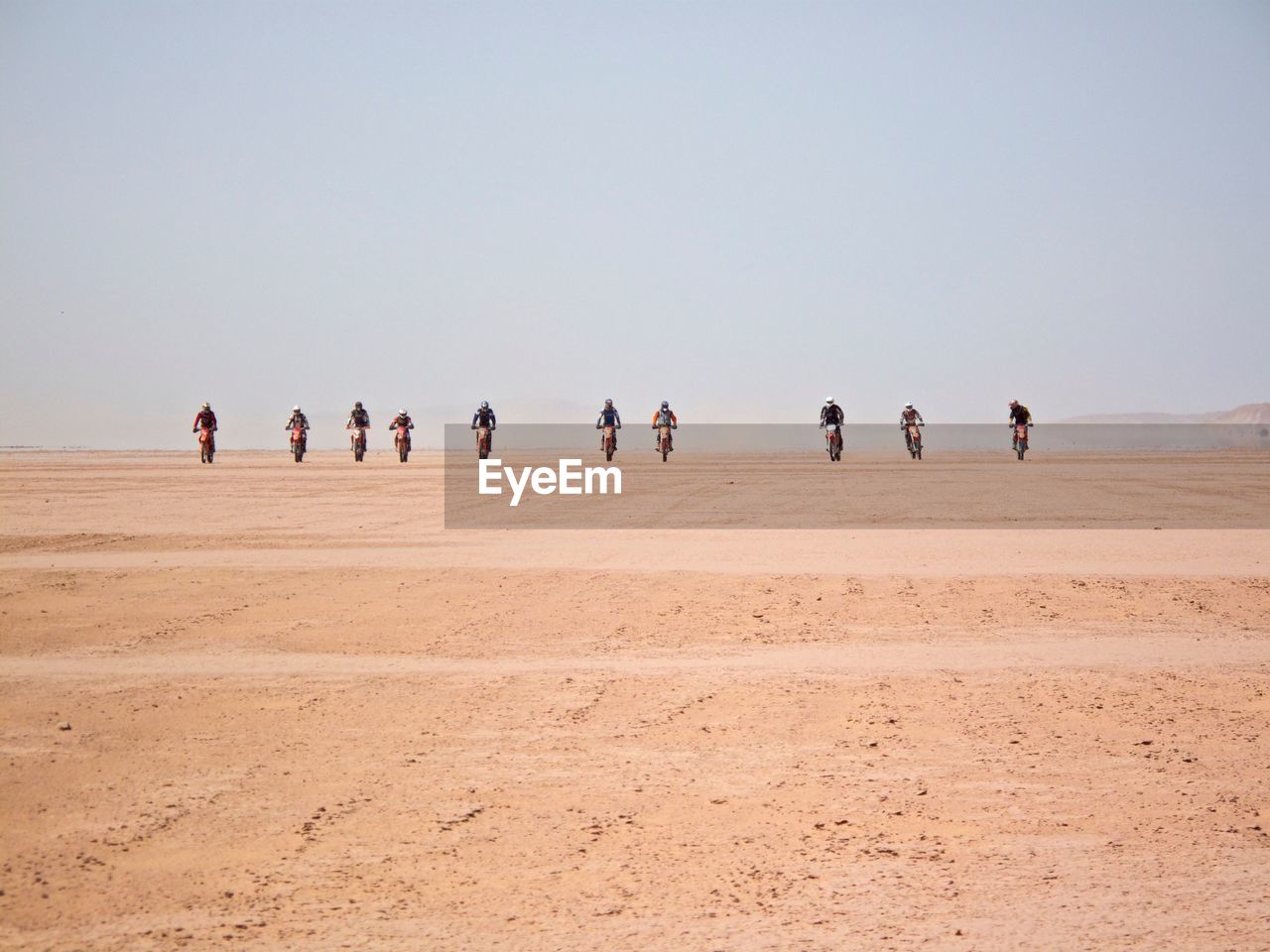 People riding dirt bike at desert against clear sky