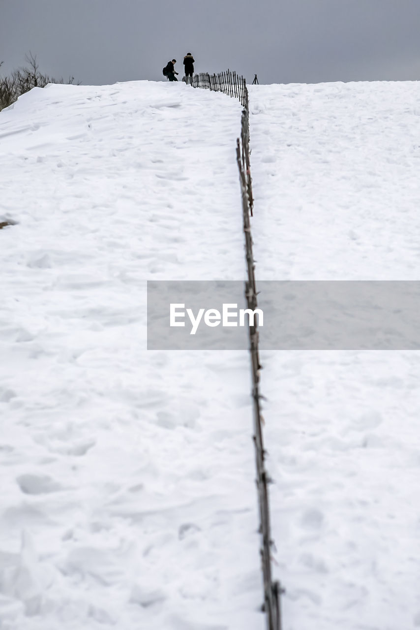 Hikers walking on snow covered hill against sky