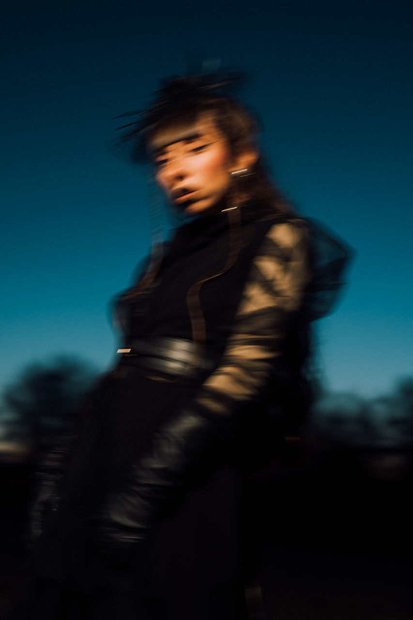 one person, blurred motion, motion, young adult, adult, sky, darkness, three quarter length, night, women, clothing, standing, nature, blue, dusk, portrait, fashion, looking, human face, side view, hairstyle, person, outdoors, speed