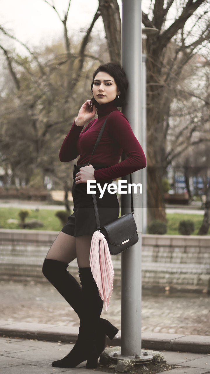 Portrait of young woman standing against pole in city