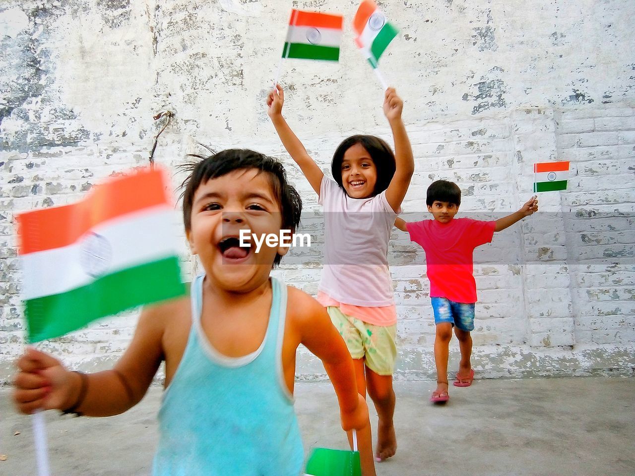 Happy siblings with indian flags running against wall
