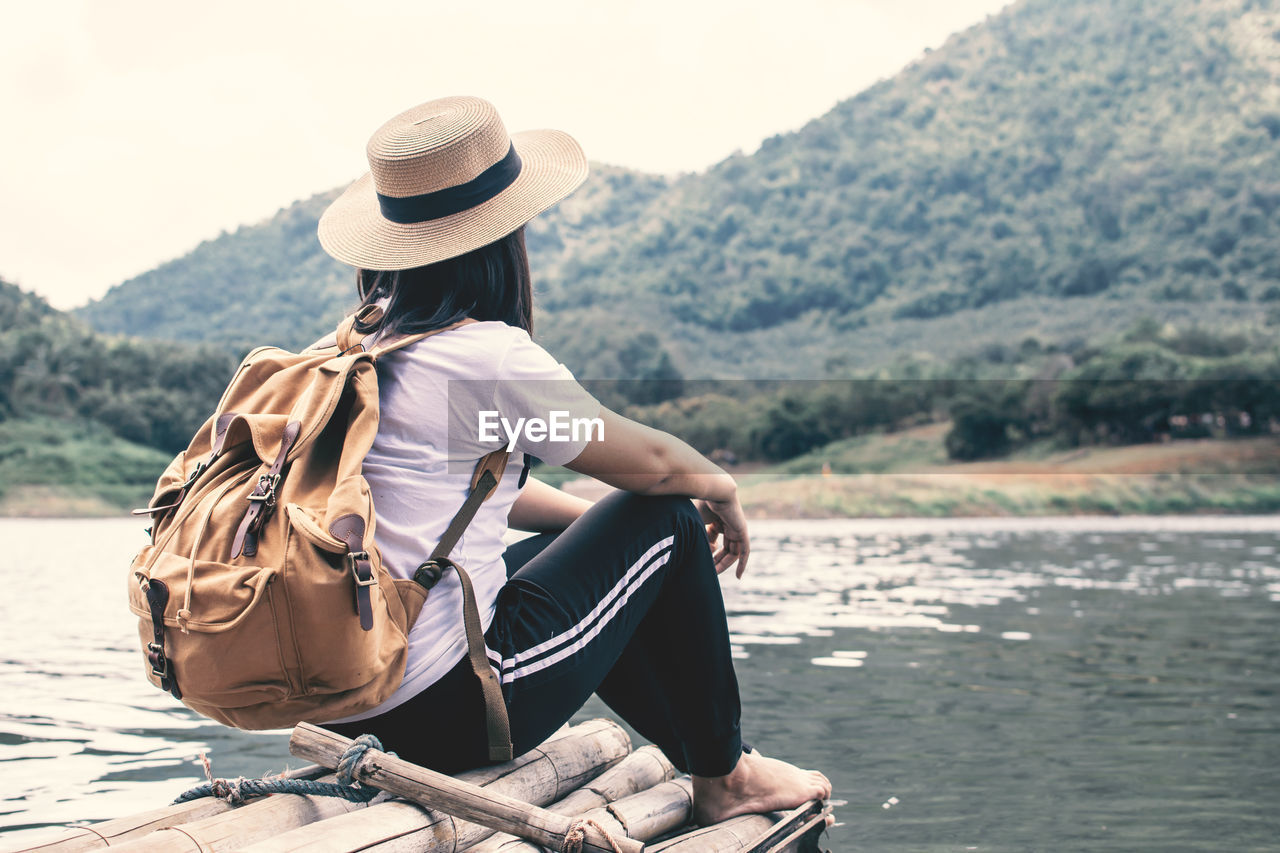 Rear view of woman sitting by lake on wooden raft