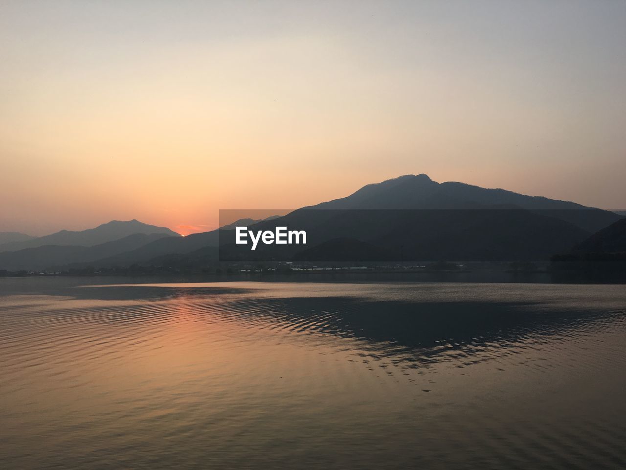 Scenic view of lake by mountains against clear sky at sunrise