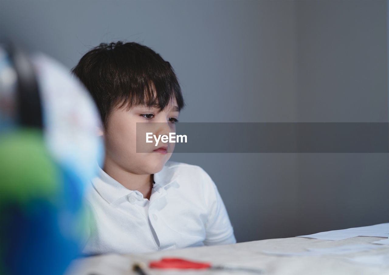 PORTRAIT OF BOY LOOKING AT CAMERA AT TABLE