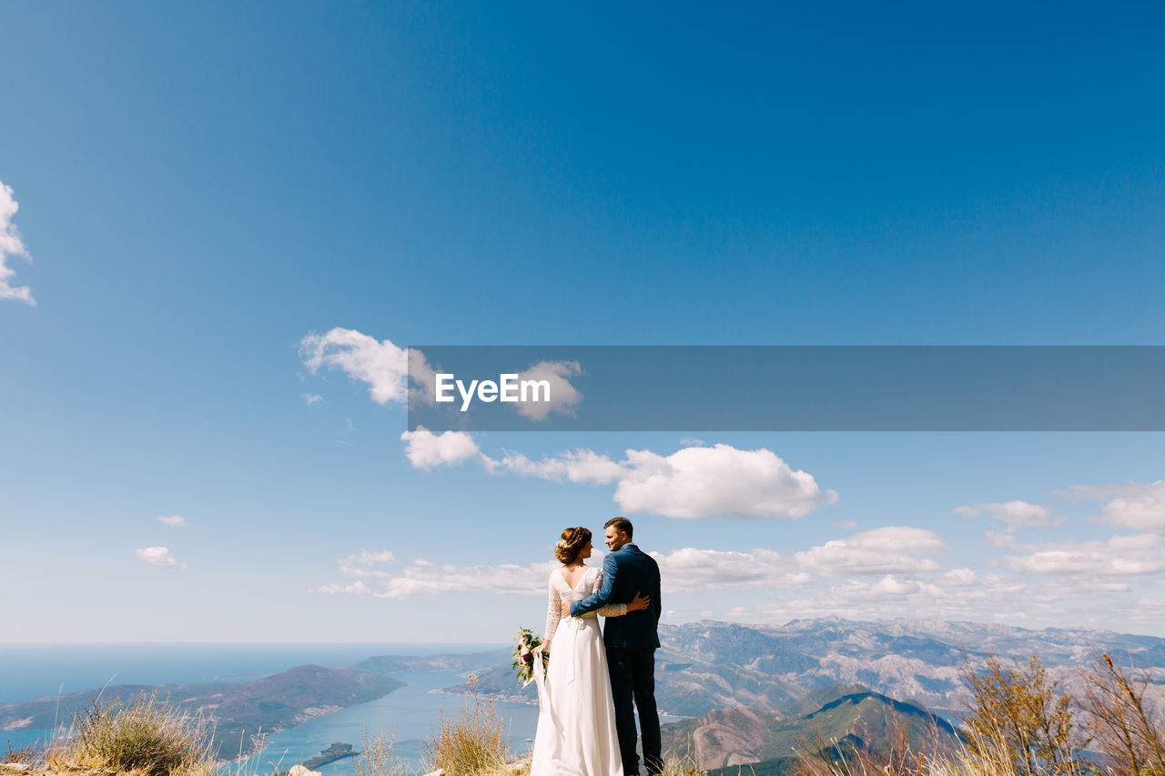 PEOPLE STANDING ON MOUNTAIN AGAINST SKY