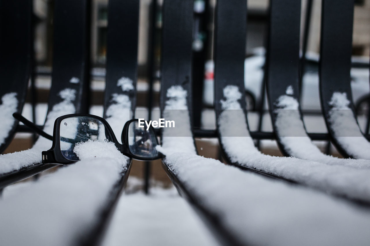 Close-up of a pair of broken reading glasses left on a snowy snow park bench 