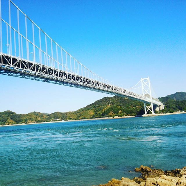 SUSPENSION BRIDGE OVER RIVER AGAINST CLEAR BLUE SKY