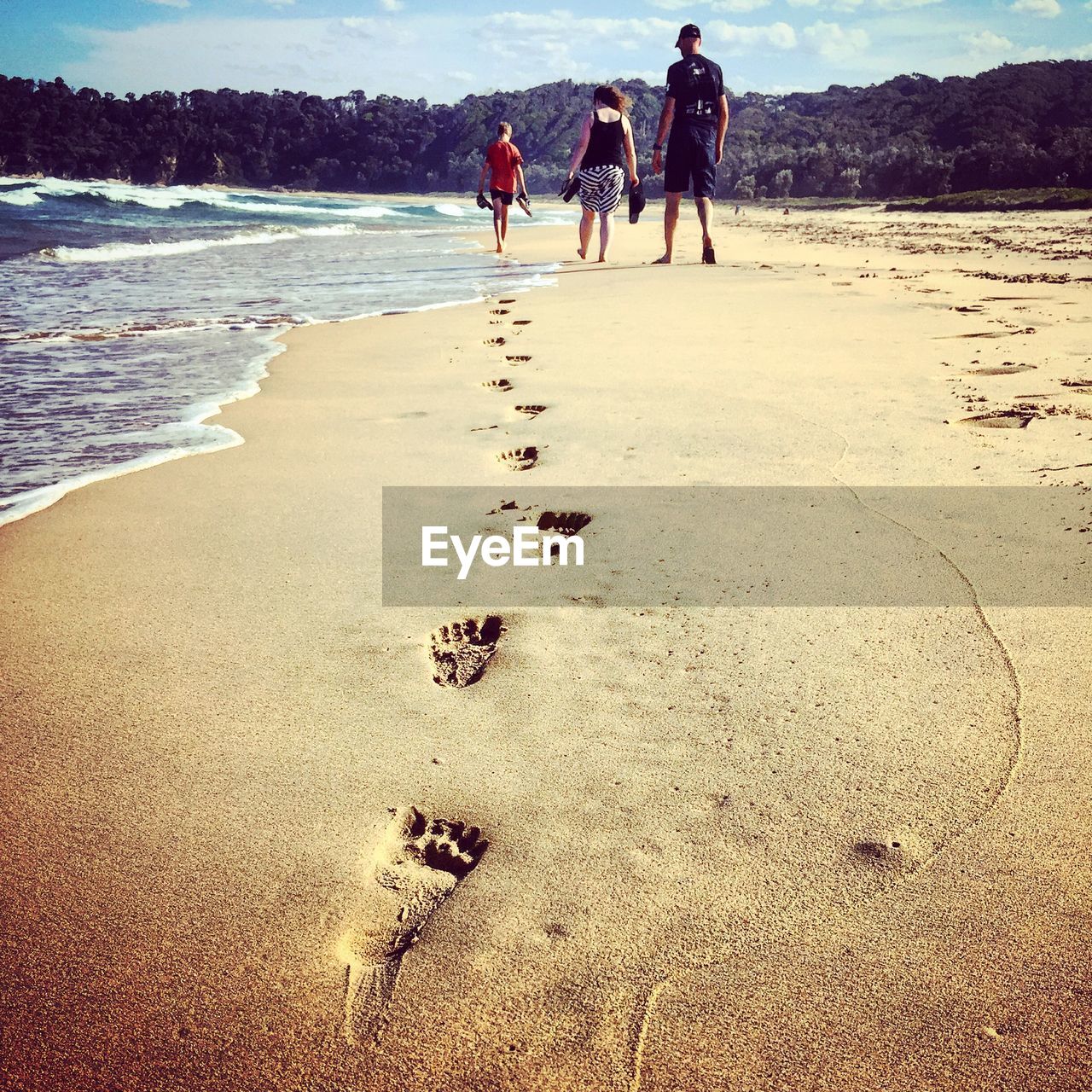 Boy making footprints while walking with parents at beach