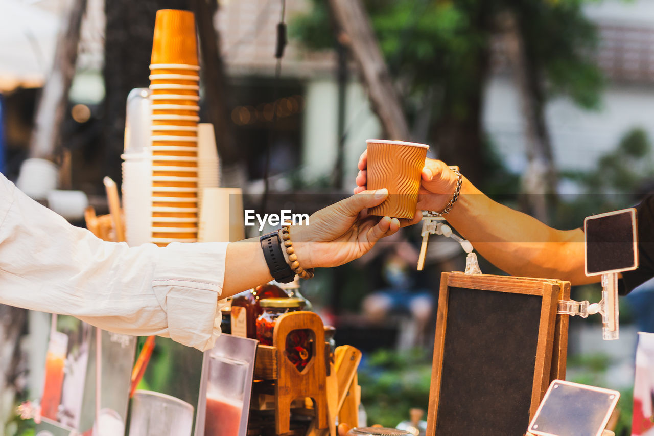 Man barista serving hot coffee in paper cup to customer over counter in cafe outdoor.