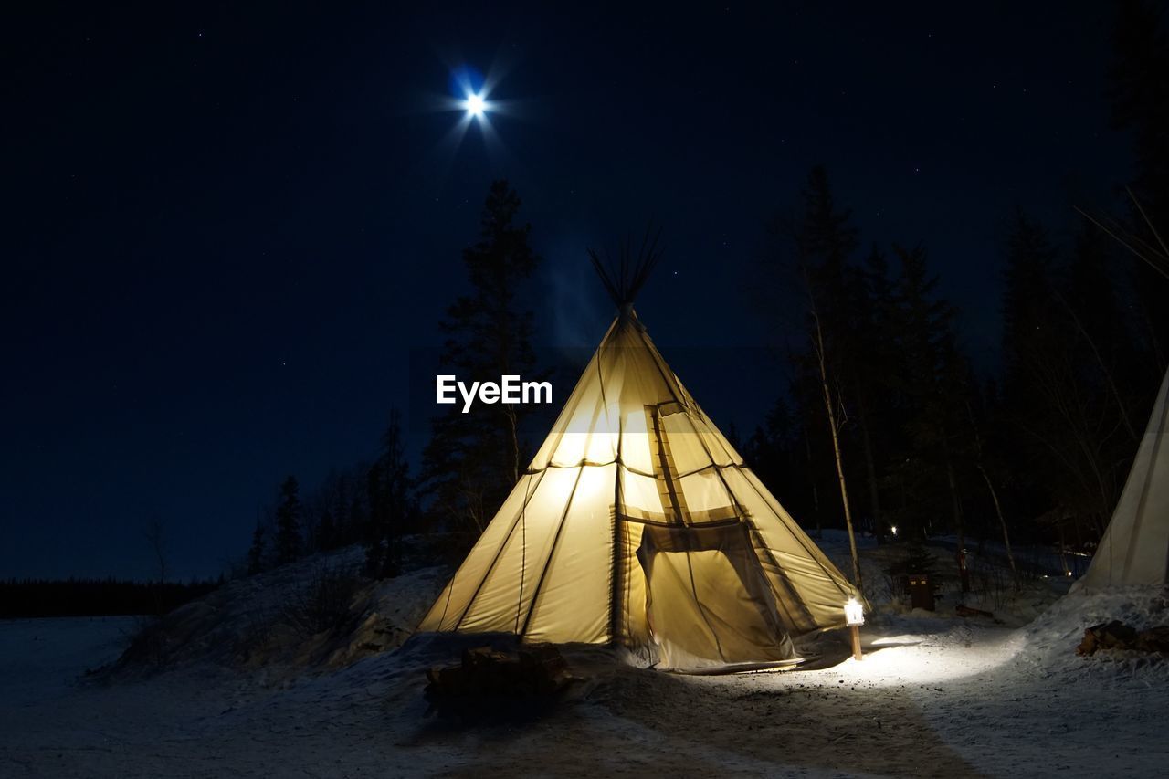 Tent on snow covered land against sky at night