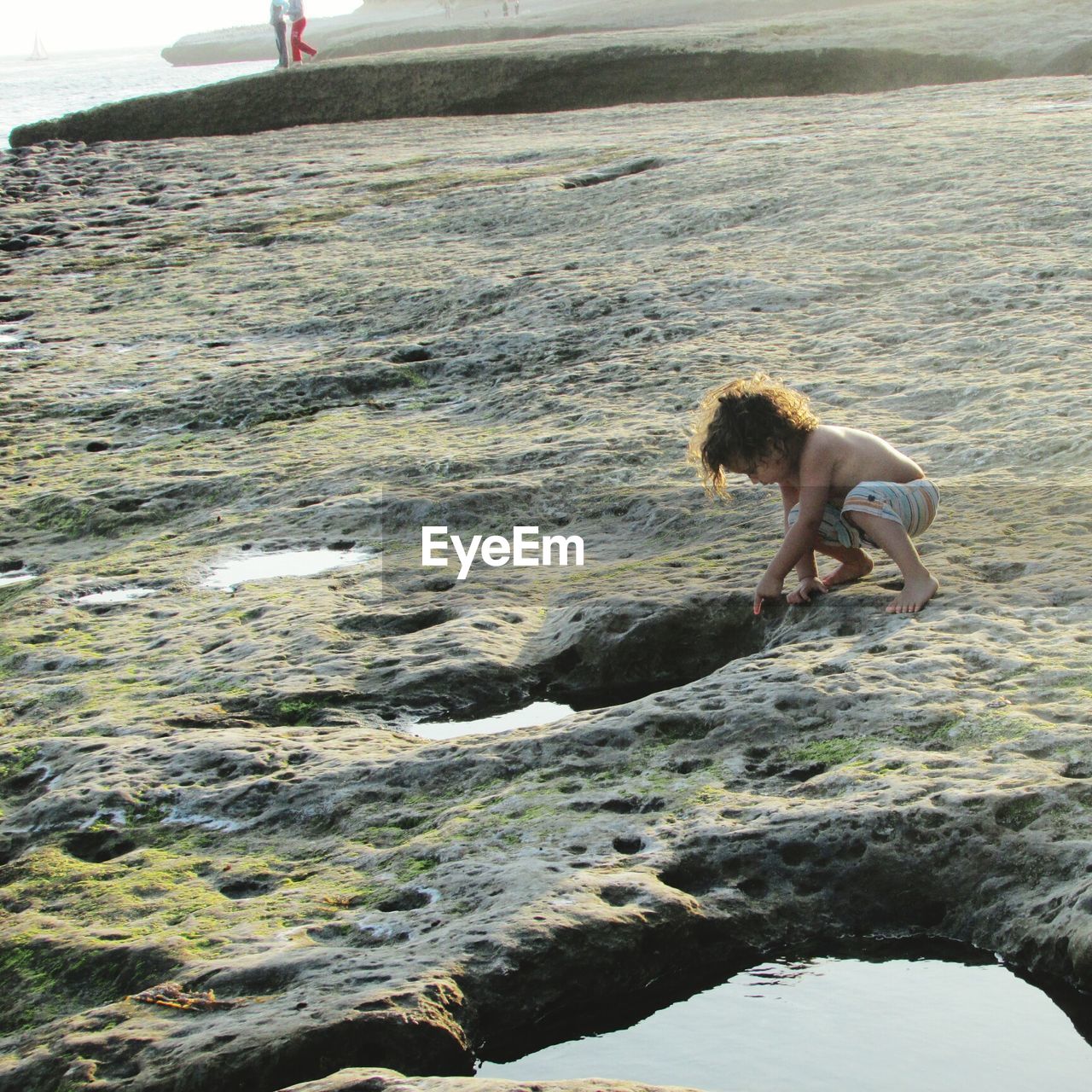 Shirtless boy by tidal pool on rock formation