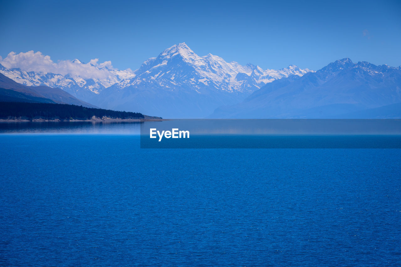 Scenic view of sea and snowcapped mountains against clear blue sky