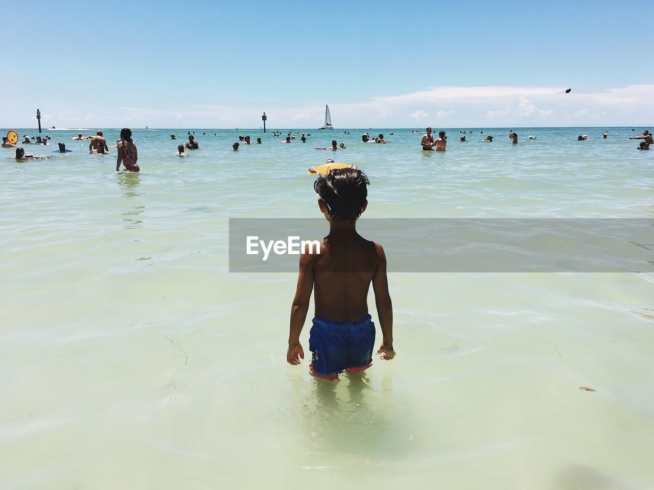 Rear view of boy standing in sea against sky on sunny day