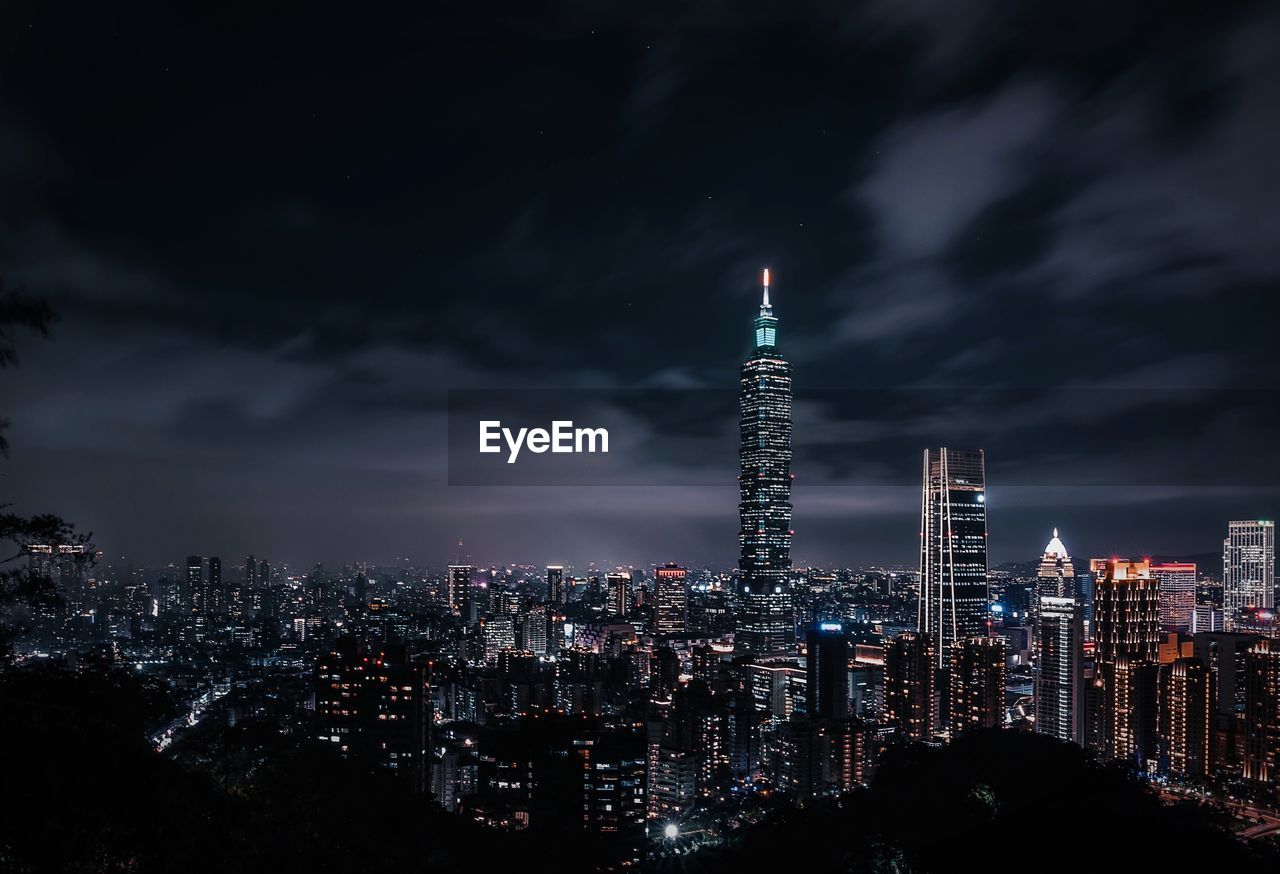 Illuminated buildings against cloudy sky at night