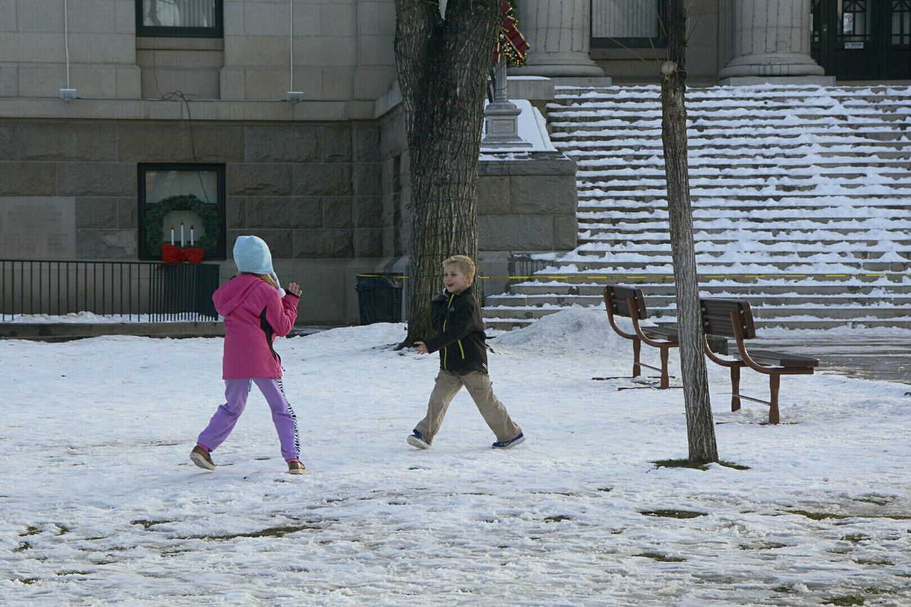 Full length of siblings playing against government building during winter