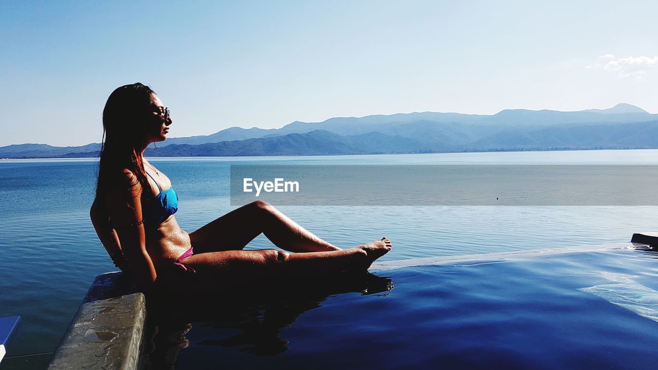 Woman relaxing at infinity pool against sky