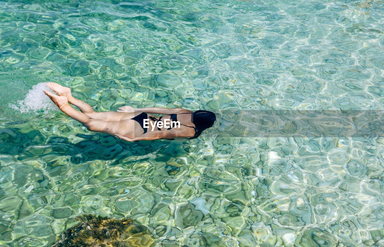 High angle view of woman swimming and diving in turquoise colored sea water.