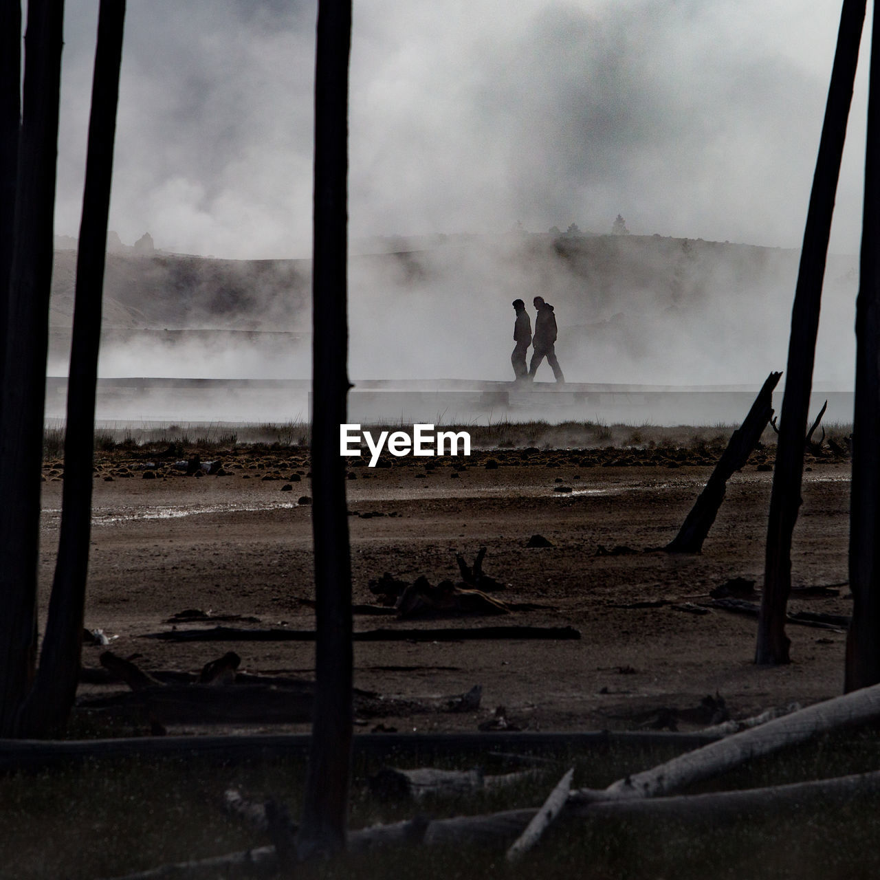 Distant view of people walking on boardwalk over geyser