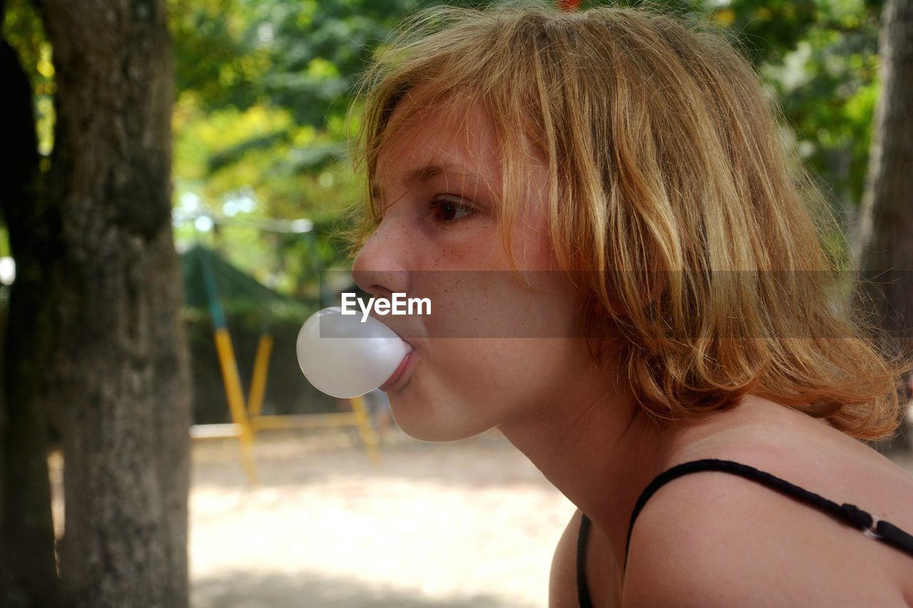 Close-up of girl blowing chewing gum by trees