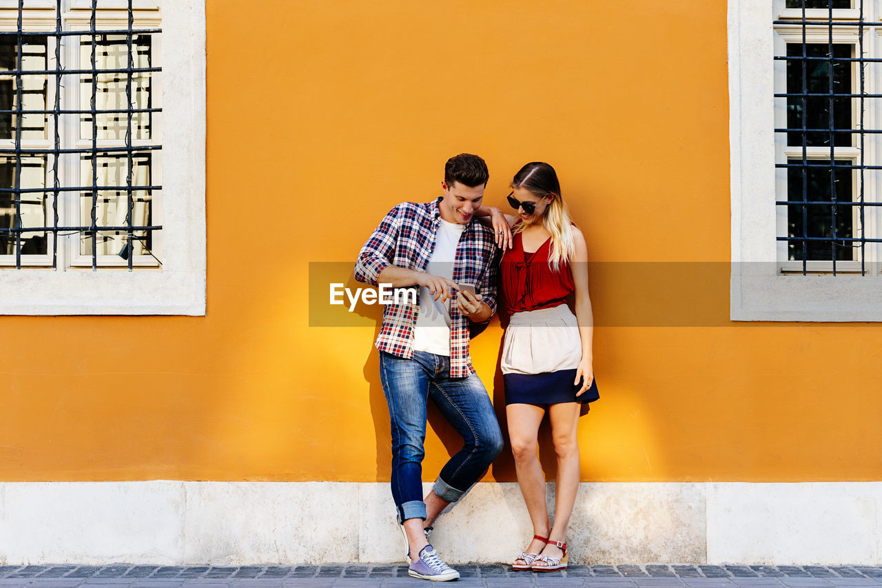 Full length of couple using phone while standing by house