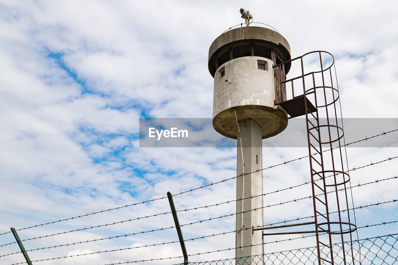 LOW ANGLE VIEW OF WATER TOWER AGAINST SKY SEEN FROM METAL FENCE