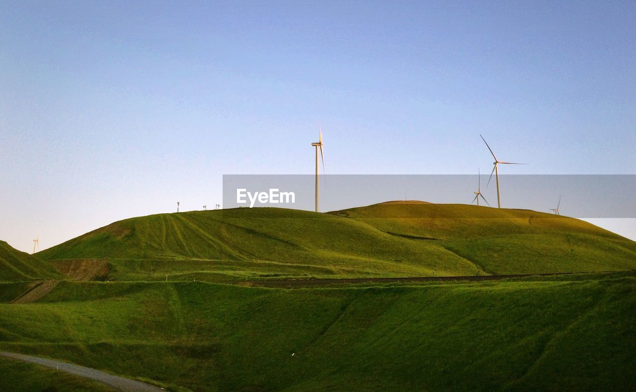 Windmills on green mountain against clear sky