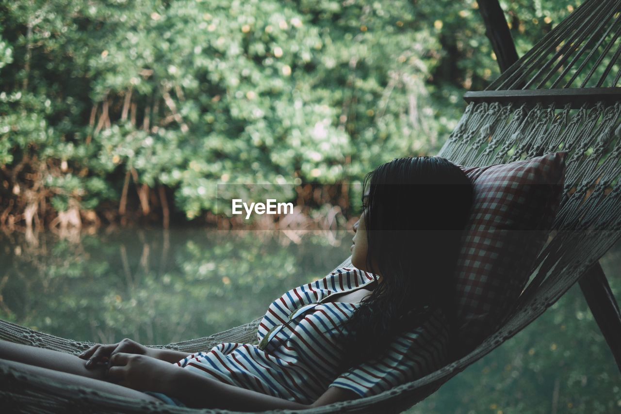 Thoughtful woman relaxing in hammock against lake