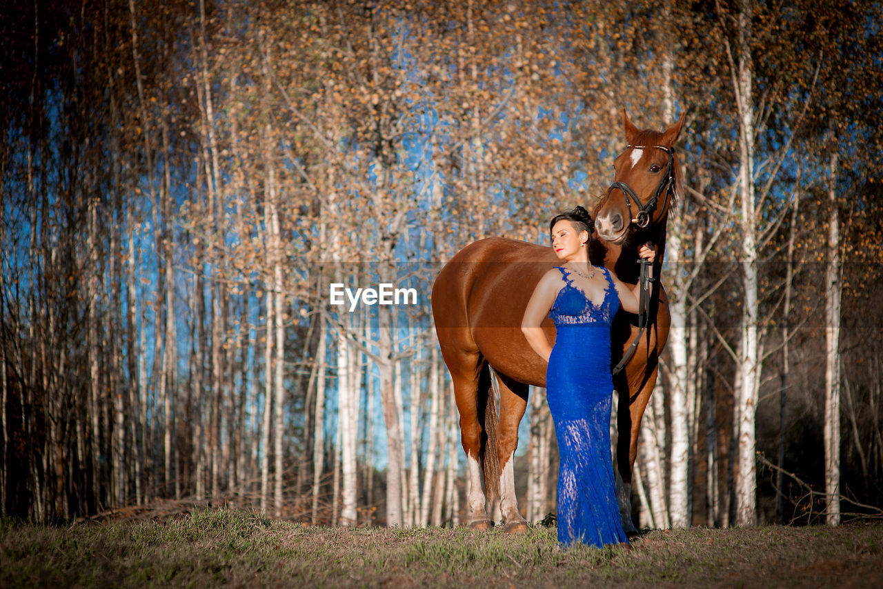 Woman standing by horse at forest