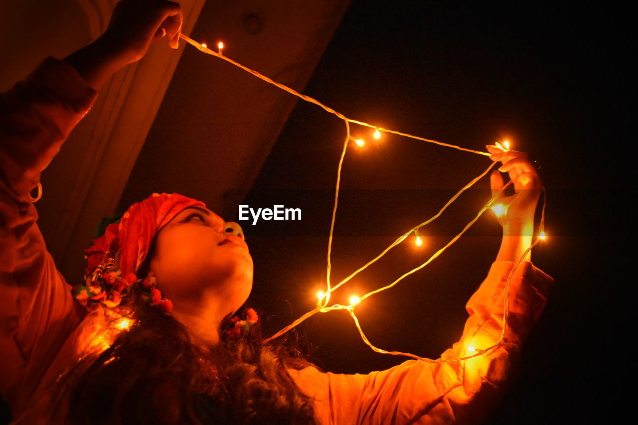Woman looking at illuminated string light in darkroom
