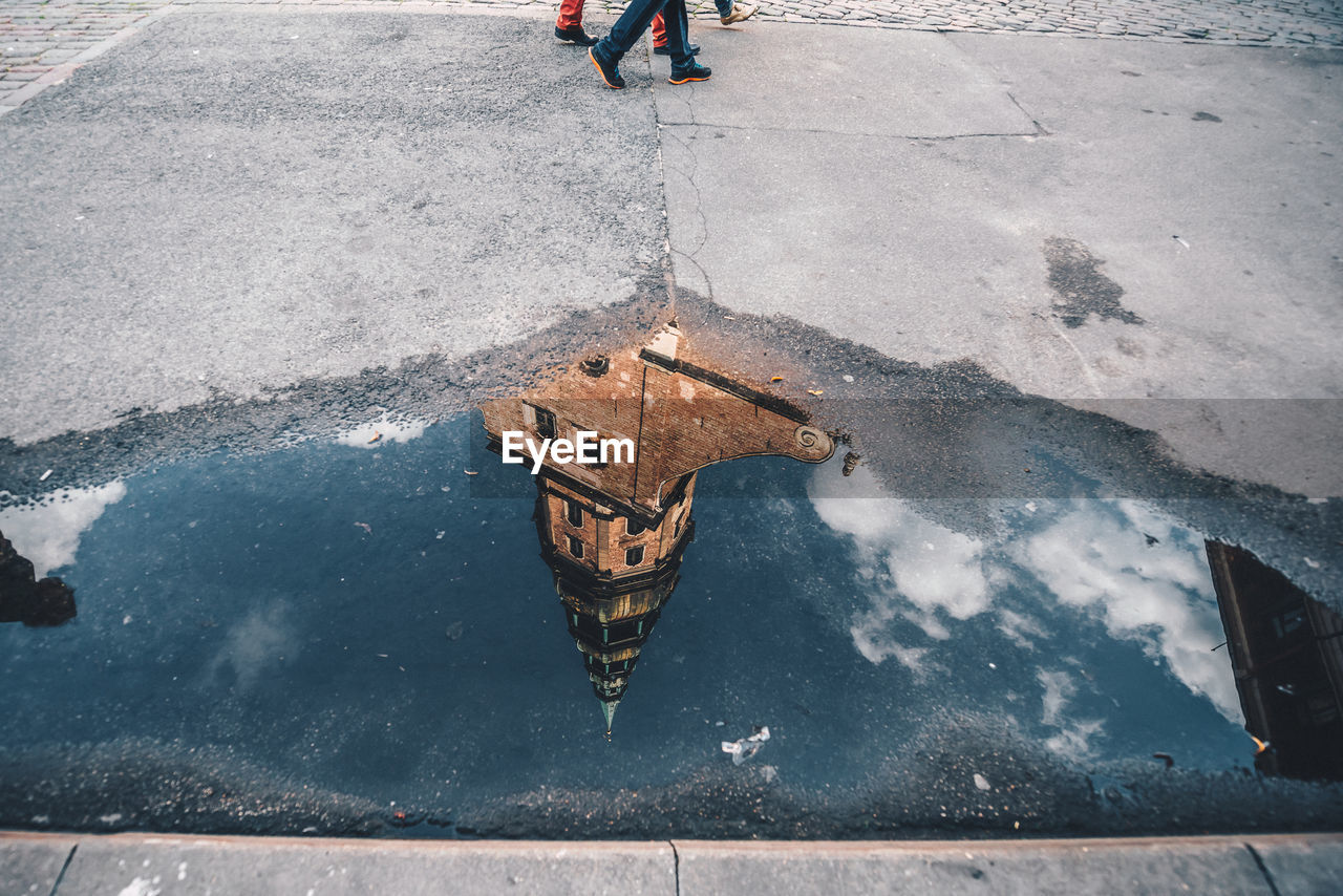 Low section of people walking on street with reflection of building in puddle