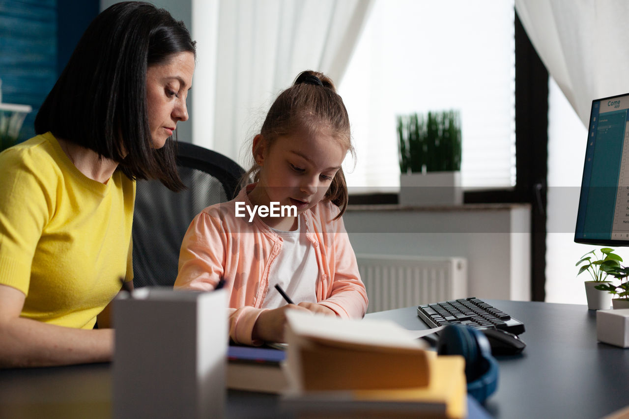 Mother and daughter sitting on table