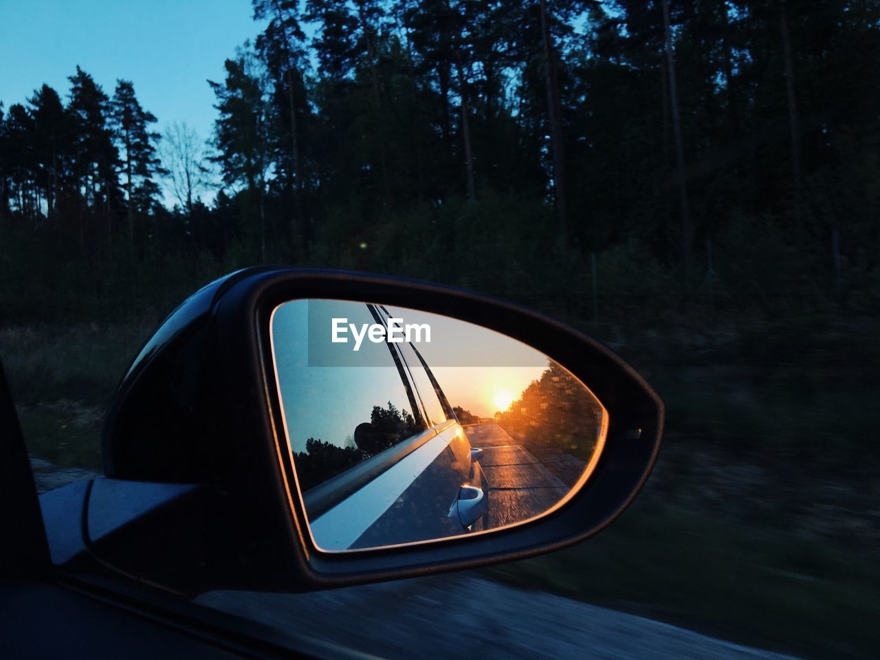 Sun reflecting on car side-view mirror during sunset