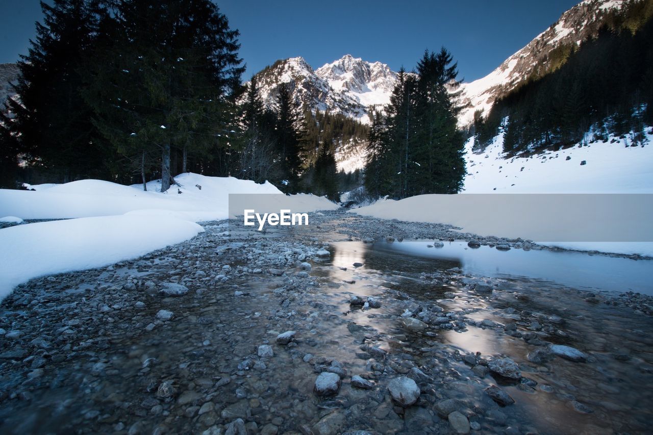 Stream flowing towards snow covered mountains