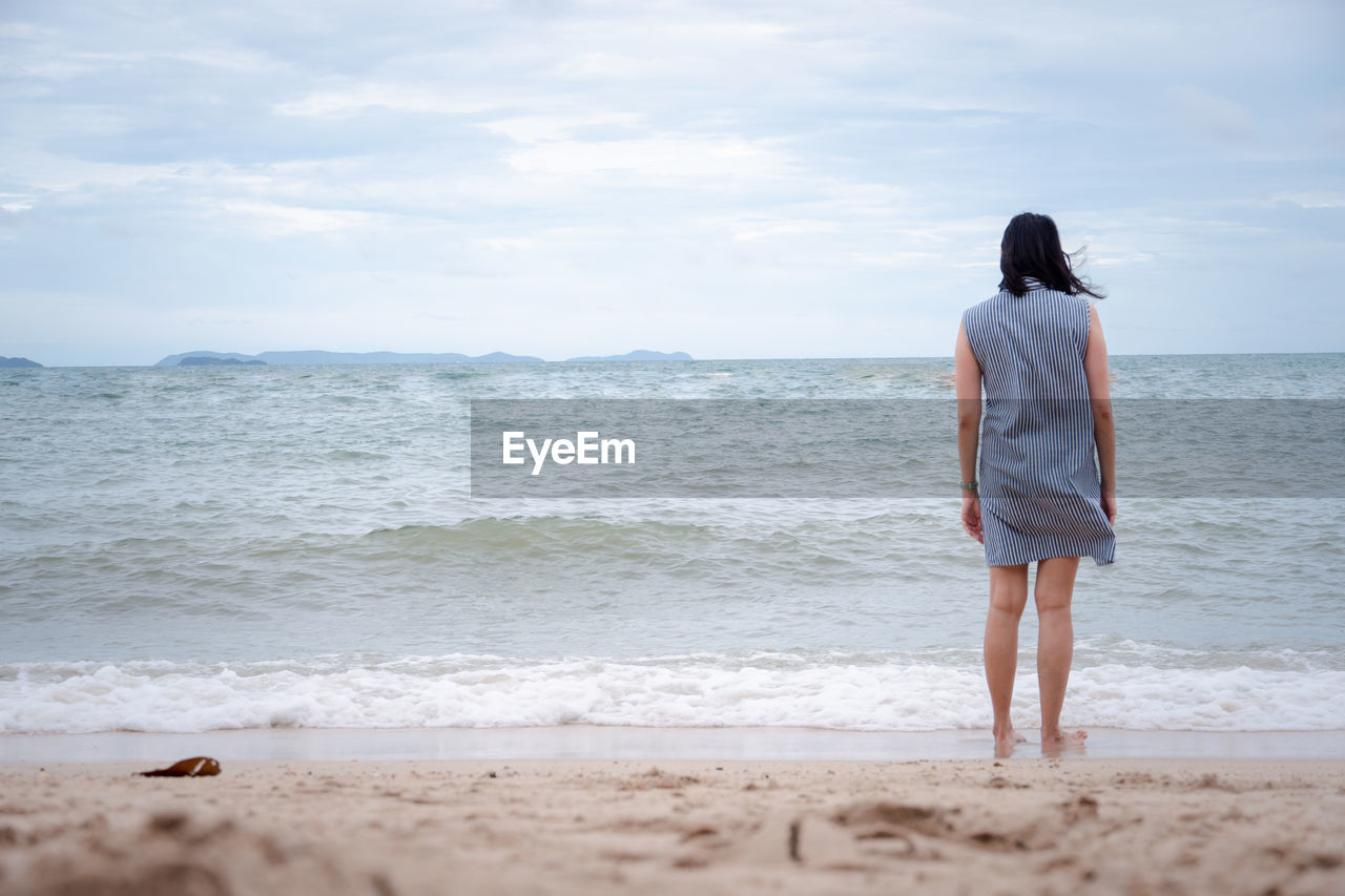 REAR VIEW OF WOMAN LOOKING AT SEA SHORE