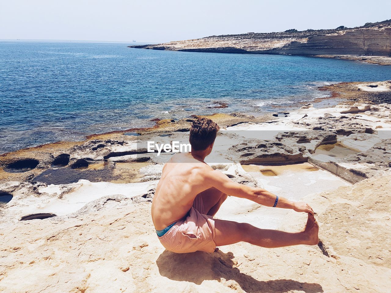 High angle view of shirtless man practicing pistol squat on rock looking at sea